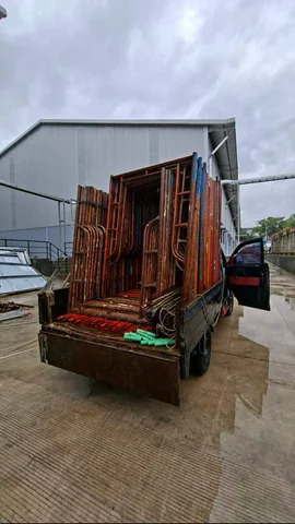 Kendaraan pick-up memuat frame scaffolding di depan bangunan gudang