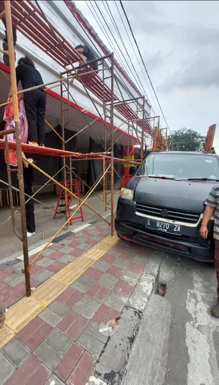 Scaffolding terpasang di fasad bangunan dekat kendaraan yang terparkir