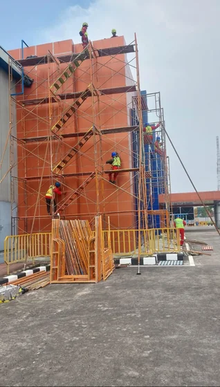 Scaffolding bertingkat terpasang di dinding bata dengan pekerja di atasnya