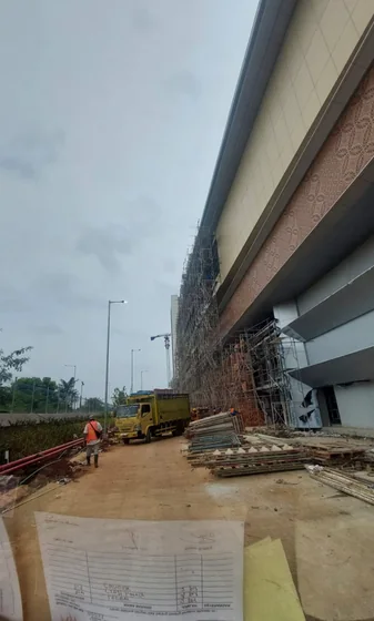 Area proyek di samping bangunan dengan scaffolding di kejauhan
