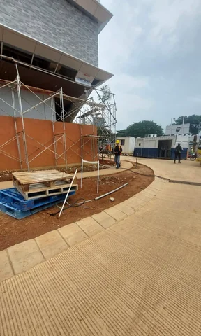 Scaffolding terpasang di sisi bangunan dengan jalur paving di depannya